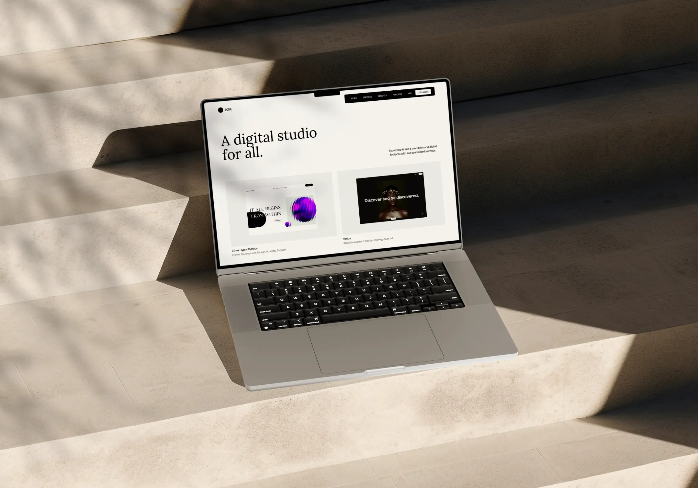 1one.studio landing page on macbook laptop that is sitting on concrete steps
